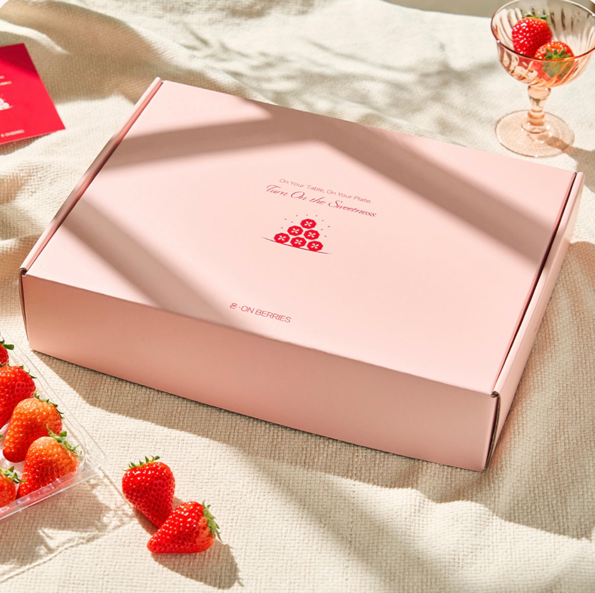 Pink gift box with printed ON BERRIES card and strawberries peeking inside