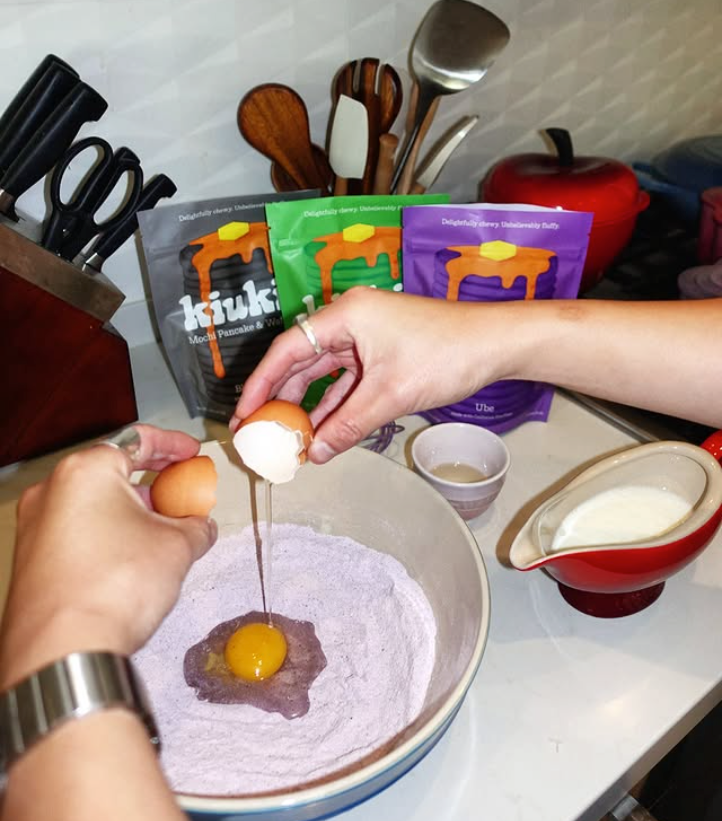 Ube mochi pancake batter with egg in a mixing bowl and red pourer