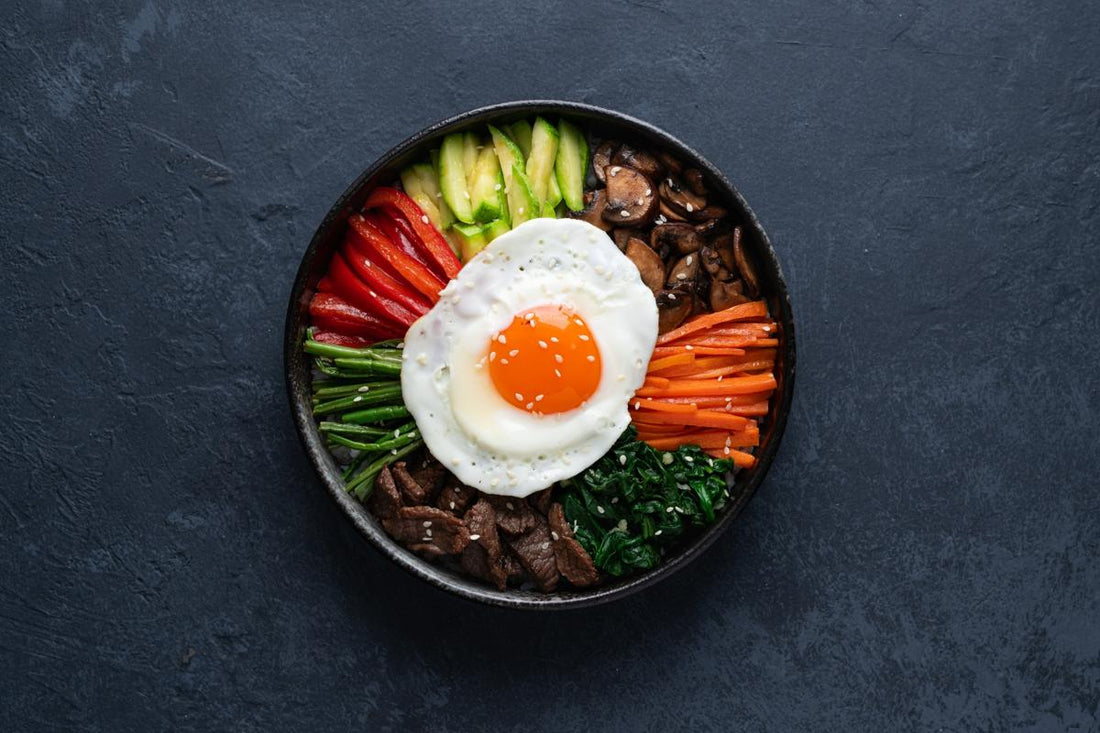 Korean bibimbap with vegetables, beef, and fried egg served in a bowl, top view on a dark background