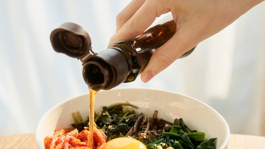 Korean sesame oil being poured over bibimbap with spring greens
