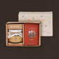 A boxed gift set from SEOGA on a dark brown background. The set includes a kraft paper box with a white jar wrapped in white paper and tied with twine, a red pouch with Korean text and a small illustration, and a tall white box behind it with a colorful grid pattern.