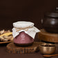 Herbal jar with maroon label, white cloth-tied lid and twine
