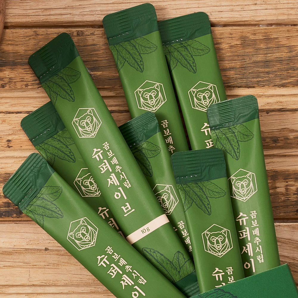 Green gombo baechu syrup sachets with leaf pattern and rose-like emblem on wooden surface.