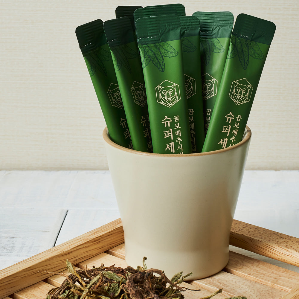 Green syrup sachets in a white container with dried herb leaves on a wooden tray.