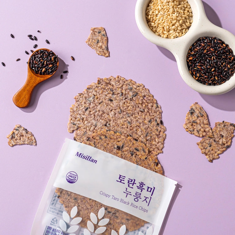 Black rice taro chips scattered around an open bag and bowls of grains