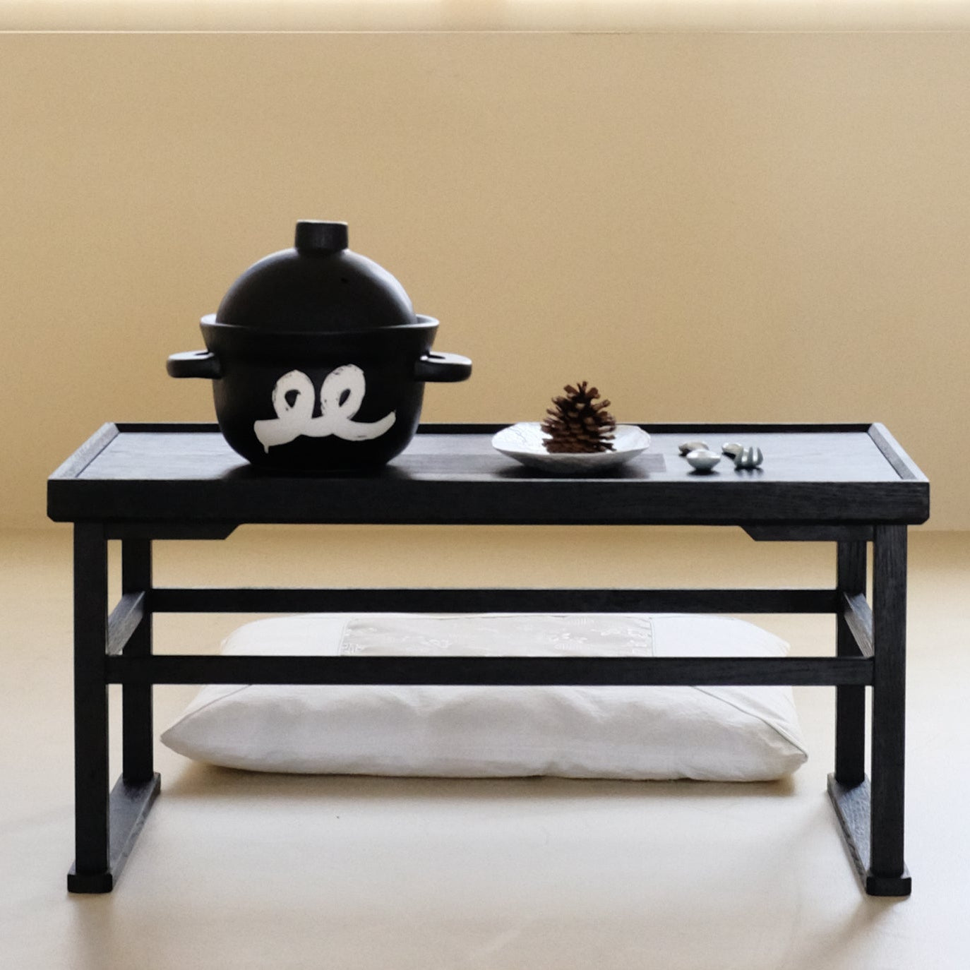 Black ceramic rice pot with lid and white emblem on a serving tray.
