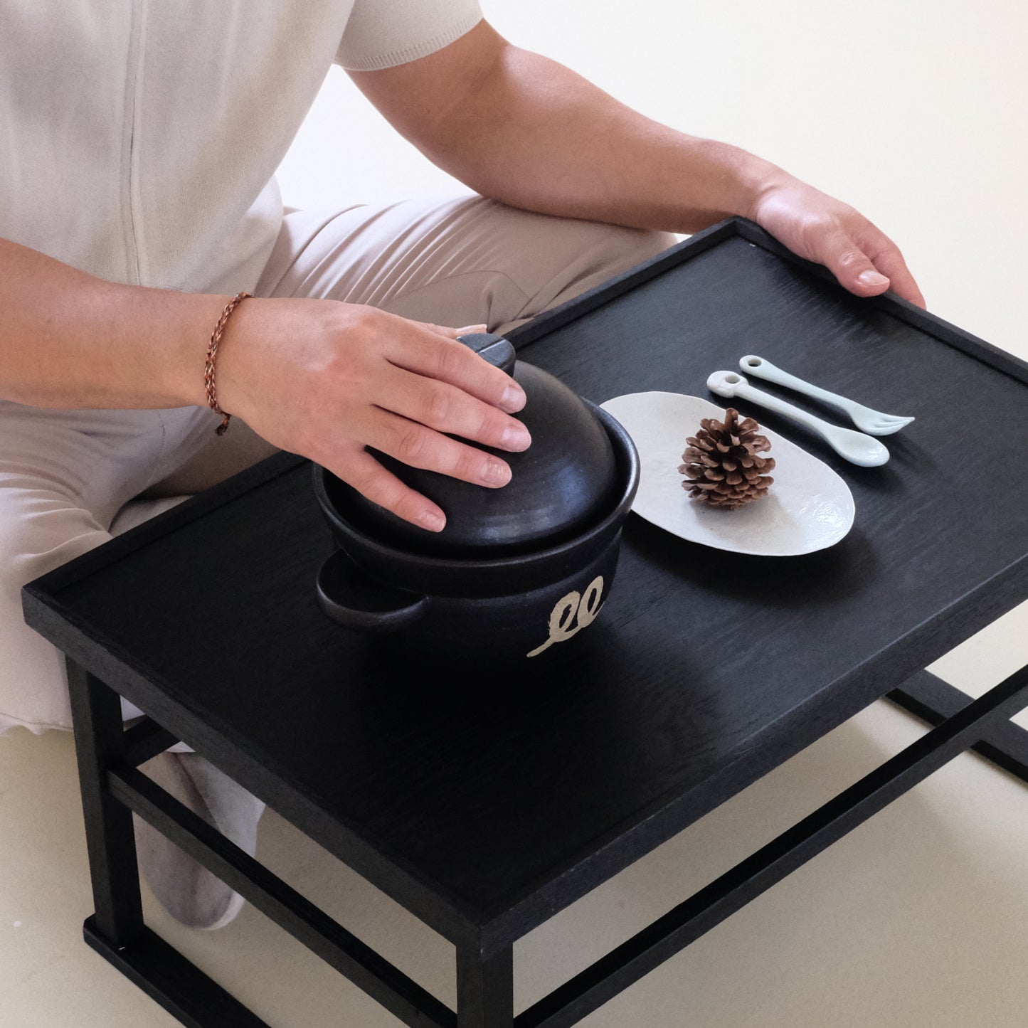 Black ceramic rice pot with lid on a tray, hands setting the lid in place.
