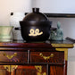 Black ceramic rice pot with lid, gold swirl emblem and side handles.