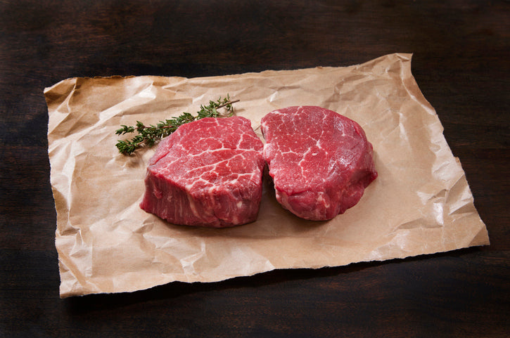 Raw steaks on parchment paper with rosemary sprigs