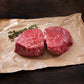Two raw steaks on parchment with a rosemary sprig