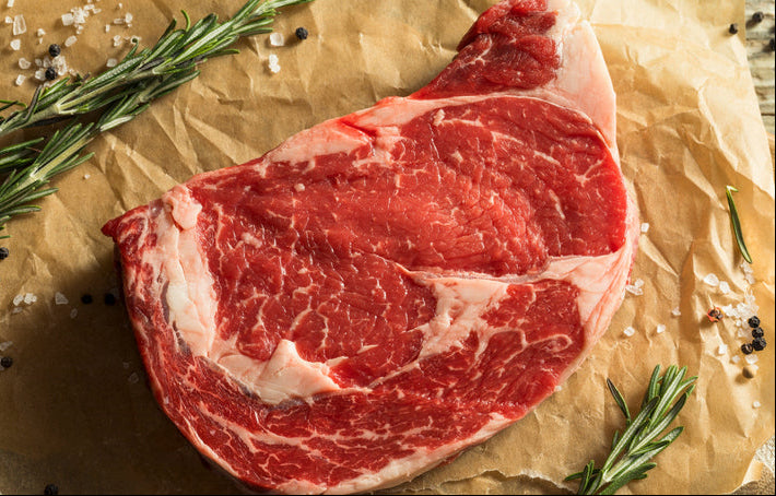 Ribeye steak on parchment with herb sprigs and pepper