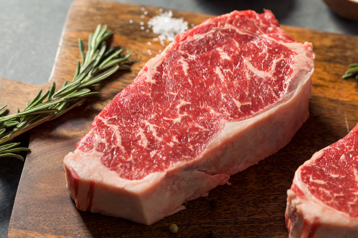 Raw red steak cut on wooden board with rosemary sprigs and pepper