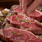 Hand seasoning ribeye steaks with herbs, sliced pieces on a wooden board