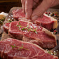 Hand seasoning raw steaks on a wooden board with herbs