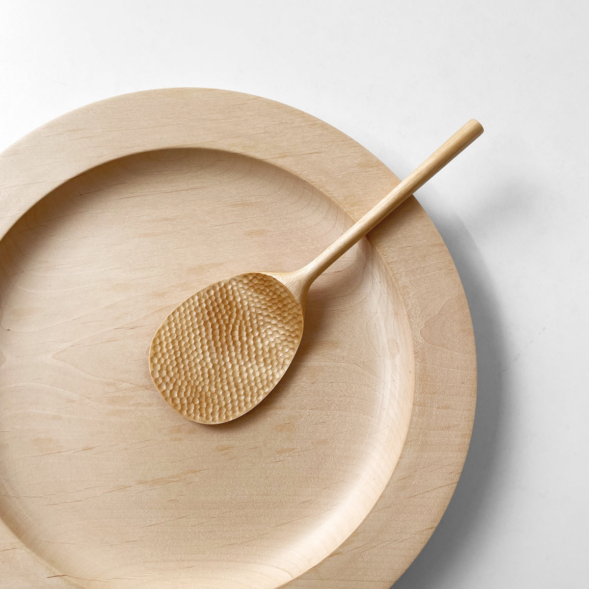 Light wood rice paddle with textured oval scoop, resting in a matching shallow bowl