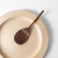 Dark wood rice paddle with textured oval scoop, resting in a shallow bowl