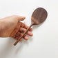 Dark wood rice paddle with textured oval scoop held in a hand
