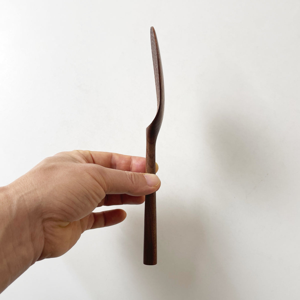 Dark wood rice paddle with textured oval scoop and long handle, side view
