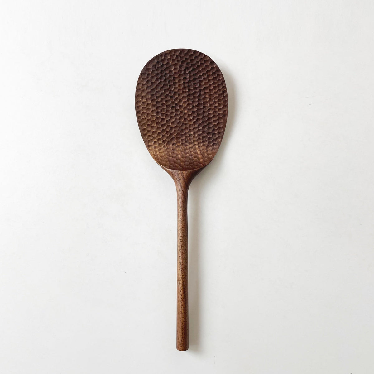 Dark wood rice paddle with textured oval scoop and long handle, standing alone