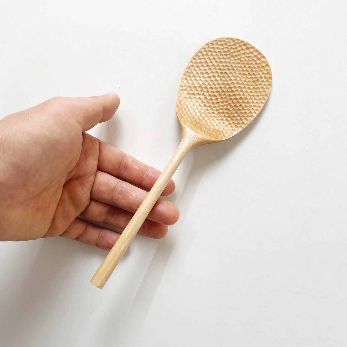 Light wood rice paddle with textured oval scoop held in a hand