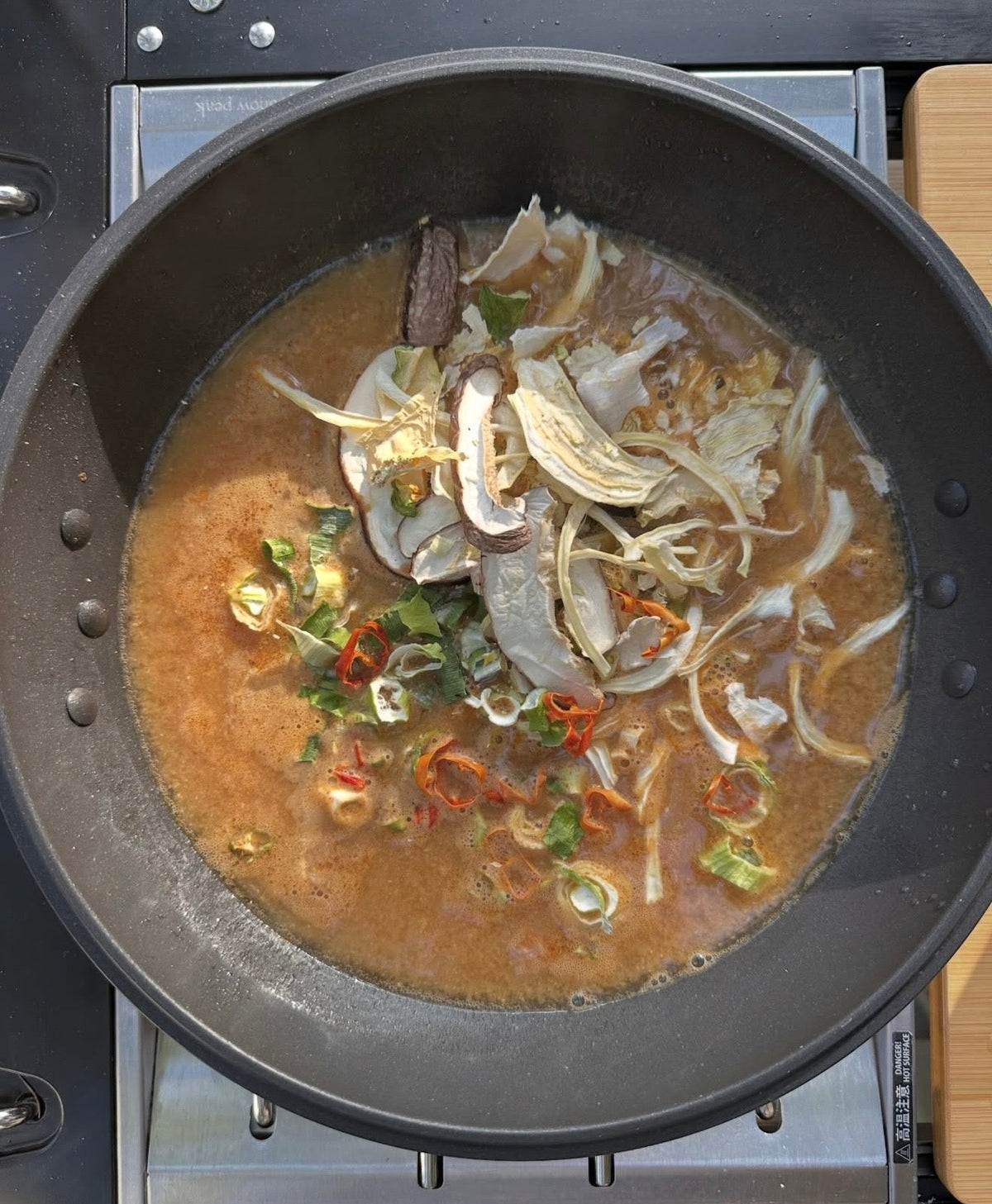 Pan of broth with sliced peppers, onions, and herbs