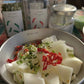Bowl of sliced vegetables topped with chopped red peppers and herbs