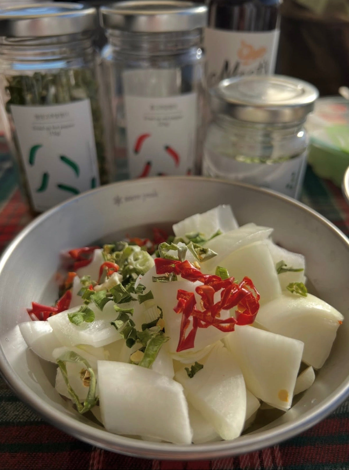 Bowl of sliced vegetables topped with chopped red peppers and herbs