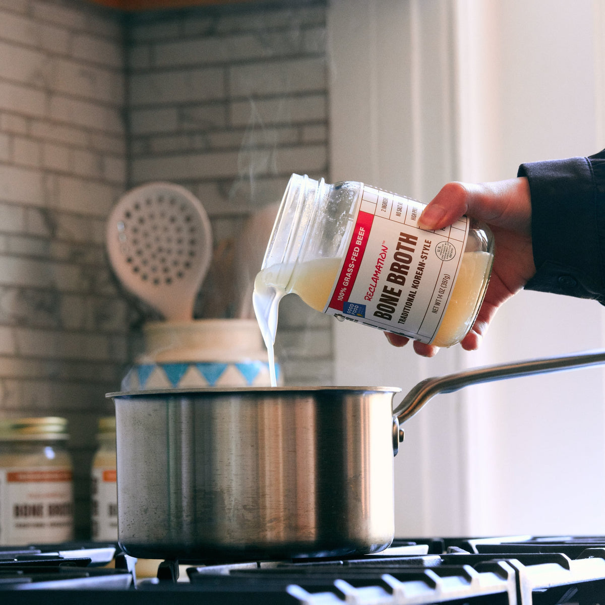 Pouring bone broth from jar into stainless pot on stovetop