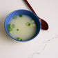 Blue bowl of pale bone broth with sliced green onions and spoon