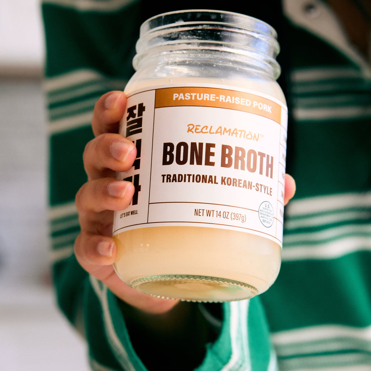 Pasture-raised pork bone broth jar held up with pale broth inside