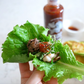 Ssamjang sauce lettuce wrap held in hand, with meat and red paste topping