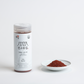 Coarse Korean gochugaru chili powder in a white jar with red powder beside it