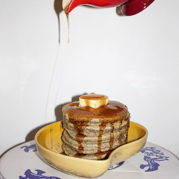 Mochi pancake stack on plate with butter square and dark syrup drizzling.
