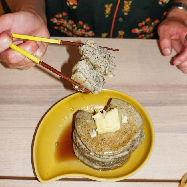 Mochi pancake stack with butter on yellow plate, chopsticks holding a piece.