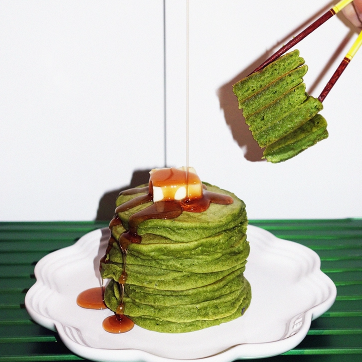 Stack of green mochi pancakes on plate with caramel drizzle and chopsticks