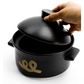 Black rice pot with lid, hand lifting the cover, gold emblem on front