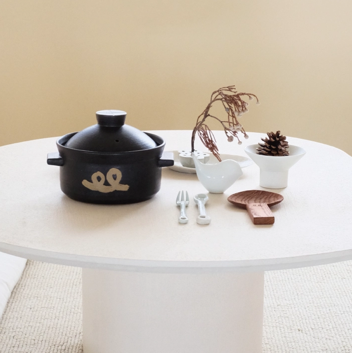 Black rice pot with lid and side handles on table, gold logo with small accessories
