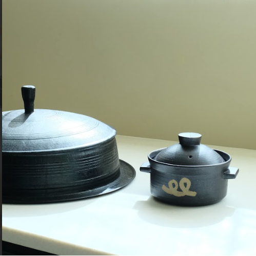 Black rice pot and covered pot with side handles, gold emblem on front