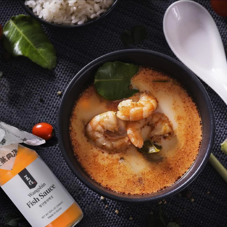 Fish (Anchovy) Sauce bottle beside a bowl of orange broth with shrimp and vegetables