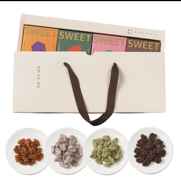 A gift box of assorted Korean sweets with four colorful candy packages visible inside, a cream-colored carrying bag with dark brown handles, and four small white plates below showing the candy varieties: candied nuts, coated candies, green candies, and raisin candies.