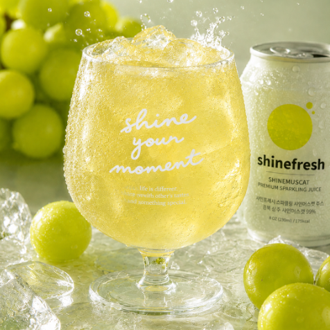 Shine Muscat sparkling juice in a stemmed glass with ice and grapes, beside a can
