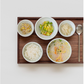 One-person white ceramic bowl set on tray with spoon and assorted servings