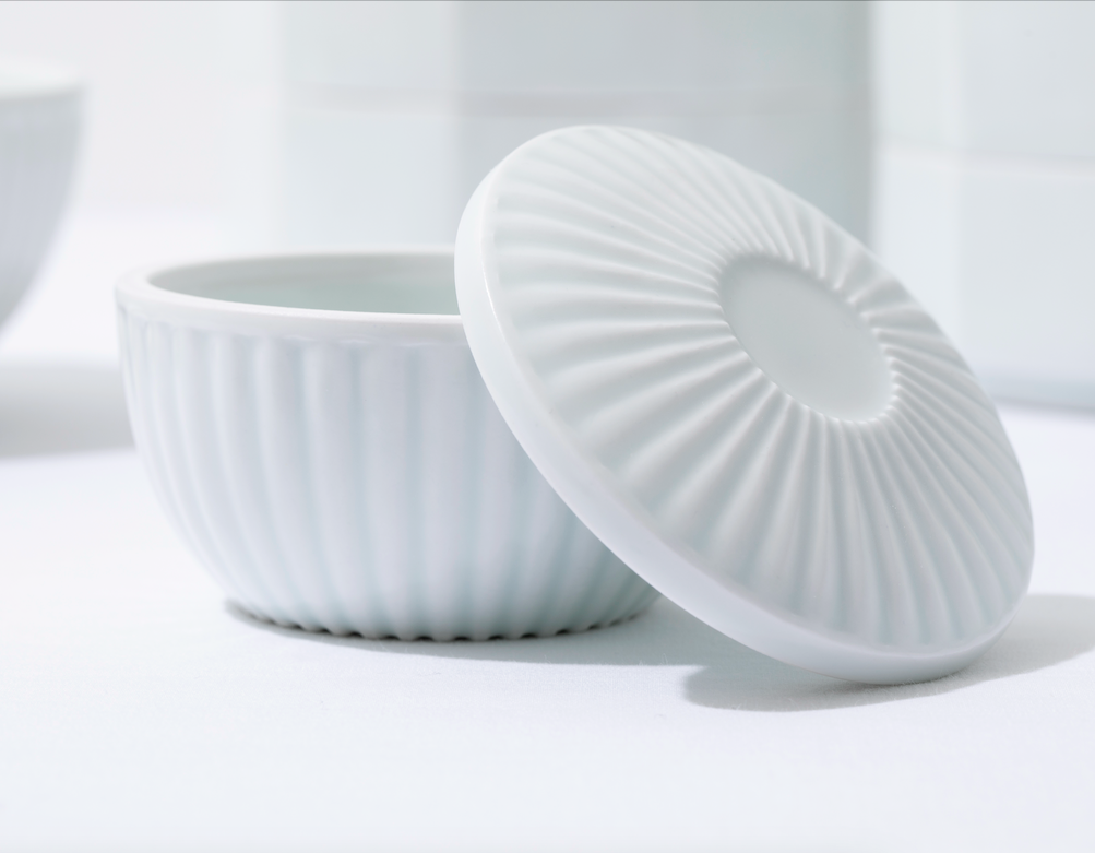 White porcelain lidded container with ribbed lid, lid leaned beside bowl