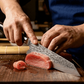 Hands slicing food with a damascus chef knife on a wooden cutting board