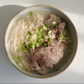 Korean-style bone broth bowl with rice noodles, sliced beef, and scallions