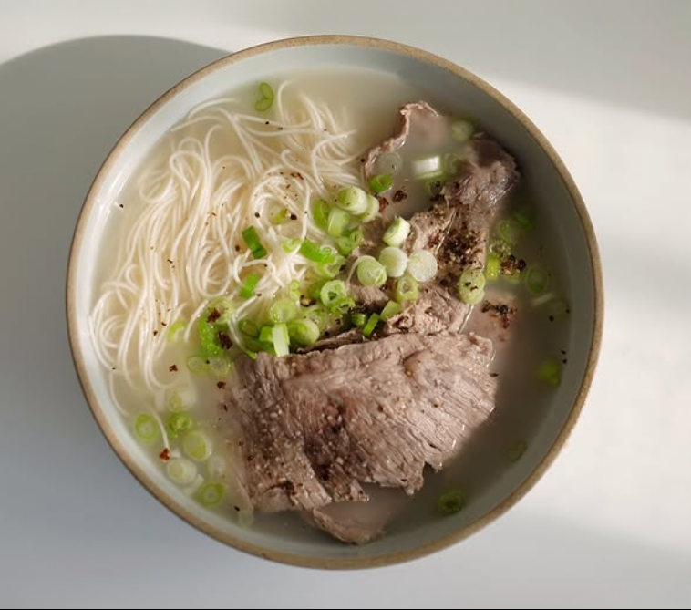 Korean-style bone broth bowl with rice noodles, sliced beef, and scallions