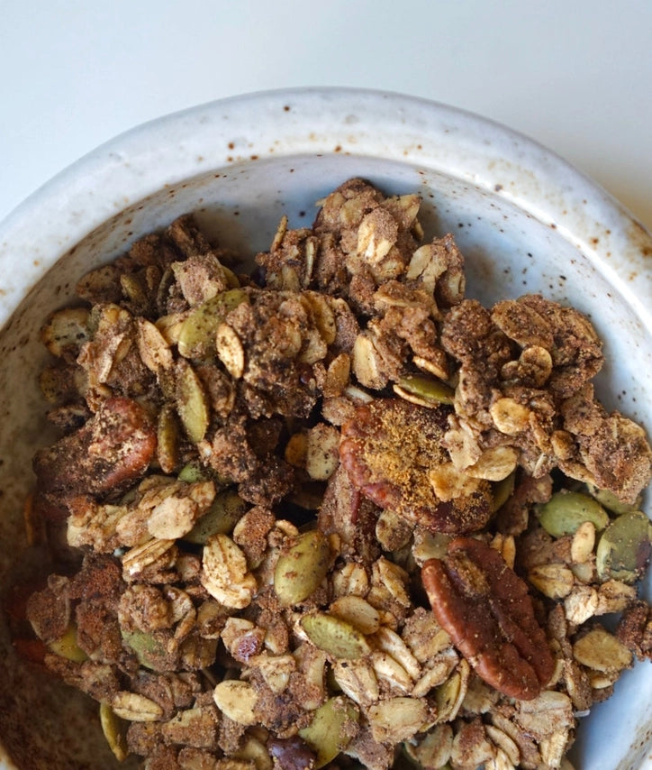 Dark granola in a speckled bowl with nuts and seed clusters