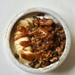 Granola bowl topped with caramel-colored sauce and sliced banana coins