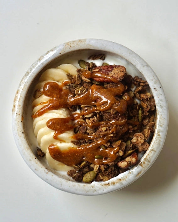 Granola bowl topped with caramel-colored sauce and sliced banana coins