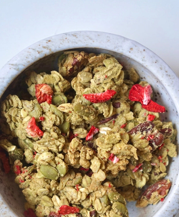 Green granola in a speckled bowl with red strawberry pieces